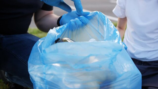 Close-up of a man with his daughter in gloves collecting garbage in the city in a blue garbage bag.