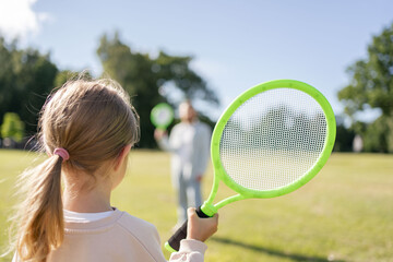 Rear view of girl holding badminton racket while playing with her father outdoors in the park on a summer day
