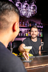 Smiling waiter offers a glass of margarita to a customer with his back to the camera