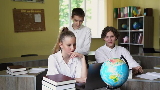 Children in school at geography lesson with globe study online on laptop and discuss different countries. Education concept 4k video. Pupils at school communicating with classmates online.
