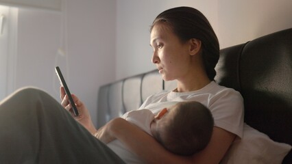 Tired young Mother is breastfeeding her baby and shopping on the mobile phone