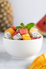 Fruit salad bowl with mango, watermelon, dragon fruit, pineapple and mint on a gray background, side view.
