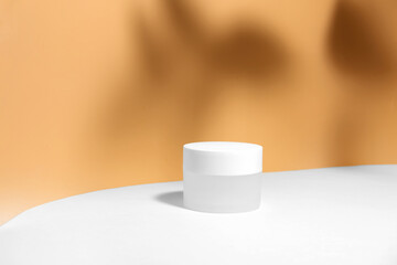 Mockup of a white jar of cream on a white-beige orange geometric gray background, on a white table with hard shadows and tropical leaves shadow. Stylish product appearance, personality.