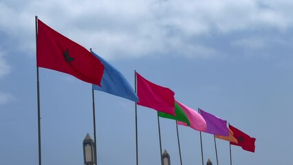 Moroccan flags alongside different colors flags fluttering with blue sky in the background