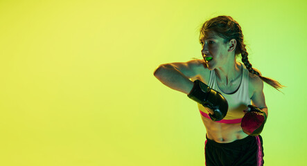 Dynamic portrait of athletic girl, MMA fighter training isolated on gradient yellow-green background in neon. Concept of sport, energy, combat sports