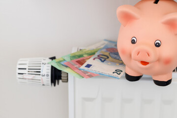 Piggy bank and euro money banknotes on heating radiator with temperature control regulator. Expensive and rising heating costs and savings energy concept
