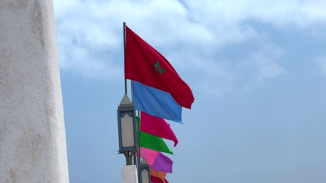 Moroccan flags alongside different colors flags fluttering with blue sky in the background