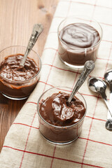 Creamy french chocolate ganache or pudding in glass on linen napkin on wooden background, three glasses