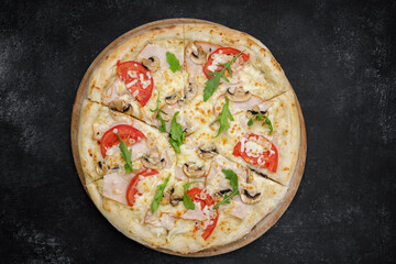 Pizza with mushrooms ham arugula, on a wooden round board on gray concrete. top view
