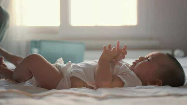 Mother is preparing to change Baby's diaper. Baby lies on back