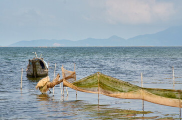 Obraz premium a fishing boat and nets are stretched on sticks against the backdrop of mountains on the horizon. Vietnamese fishing boat