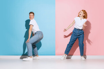 Obraz premium Portrait of young emotive couple, cheerfully dancing, posing isolated over pink blue studio background