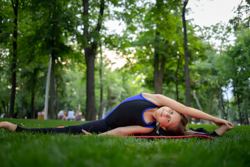a girl in the park stretches Nogina Ida in the side and holds out her hand; she practices yoga