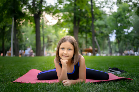 in the park, a little girl performs a frog element, doing stretching on a mat