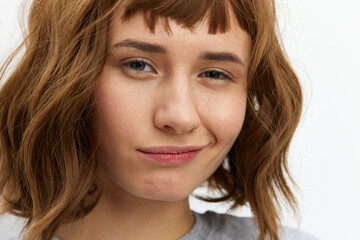 Naklejka premium a cute, playful woman stands on a white background and looks at the camera with a funny look. Close horizontal photo