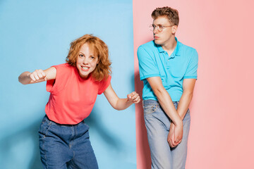 Portrait of young couple, emotive, active woman and shy man posing isolated over pink blue studio...
