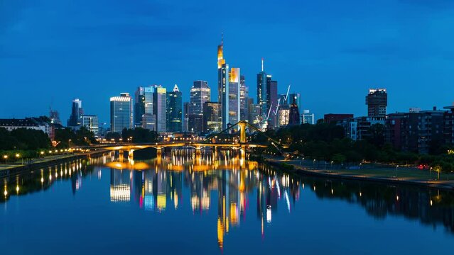 Night to Day Sunrise Frankfurt skyline time lapse, blue sky with clouds, office buildings and skyscraper in center with river and bridges in the foreground, Frankfurt am Main, Hessen, Germany