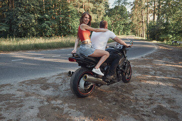 Fototapeta na wymiar A young happy couple rides a motorcycle on an asphalt road in the forest, freedom and travel, in motion