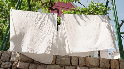 A close-up of a white cloth dries on a rope under the sun outside against the backdrop of trees in the resort town. Close up