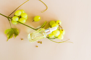 the top view of the cosmetic transparent bottle with organic product on the grape seeds lies on clusters of green grapes. beige background.