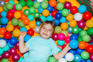 Fototapeta na wymiar a smiling child in a sea of balloons.a little happy girl is playing with colored balls in the game center
