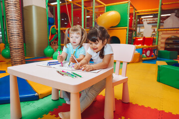 little girls are sitting at a table and drawing in a children's play center. children's creativity