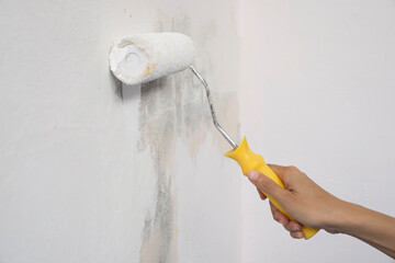hand worker holding brush painting roller white on the wall house, diy and repair concept
