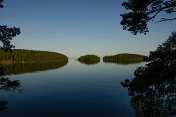 Fototapeta na wymiar Islands with green forest calm lake water against blue sky