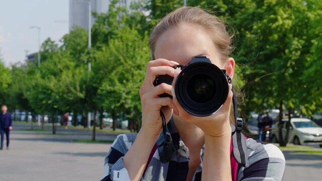 Positive girl takes pictures of sightseeing attractions while travelling in strange city or country. Young woman smiling, shooting urban landmarks. Front view. Wedding female photographer