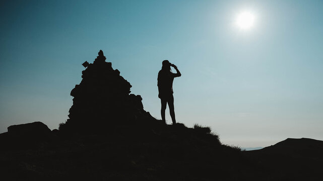 Silhouette of woman standing on rock near the edge of mountain on background of sky