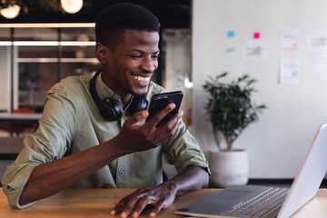 Smiling african american young businessman talking through smart phone speaker in office