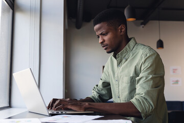 Determined african american young businessman working on laptop in creative office