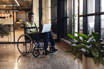 Fototapeta na wymiar Happy african american businessman with disability using laptop in wheelchair at workplace