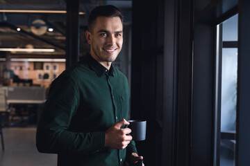 Portrait of smiling caucasian young businessman with coffee cup at creative office