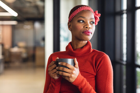 Thoughtful african american businesswoman with coffee mug looking away in creative office