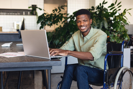 Portrait of smiling african american businessman with disability using laptop in wheelchair