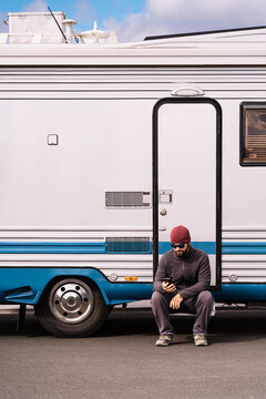 Young male tourist using smartphone sitting near trailer on road