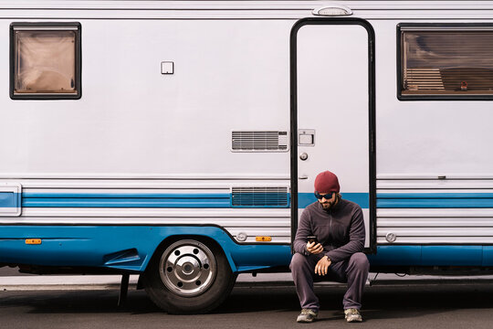 Young male tourist using smartphone sitting near trailer on road