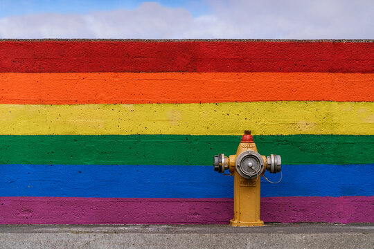 Fire hydrant on asphalt road near wall with rainbow flag