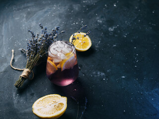 A glass of lavender lemonade with lemon on a dark table. Refreshing craft drink