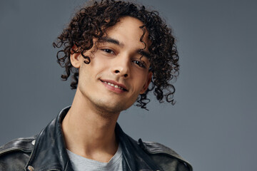 Headshot portrait of stylish tanned curly man leather jacket posing isolated on over gray studio background. Cool fashion offer. Huge Seasonal Sale New Collection concept. Copy space for ad