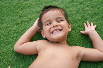 Close up of a happy smiling little brunette boy is playing on the green grass.