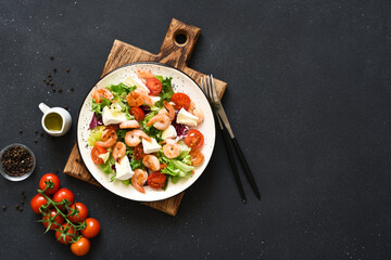 Mix salad with shrimp, brie cheese and tomato sauce on a black concrete background, top view.