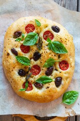 Fresh Italian flat bread Focaccia with tomatoes, olives, garlic and herbs on a wooden background.