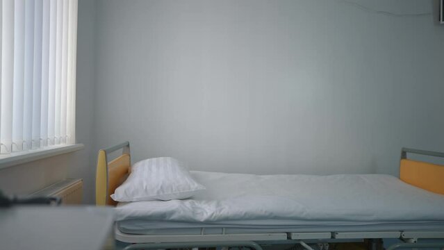 Panning shot of clean white hospital bed in modern medical clinic indoors. Live camera moving left to right along comfortable furniture in hospital with no people. Service and health care concept