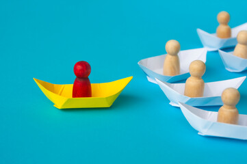 Red wooden figure on yellow paper ship origami leading the rest.