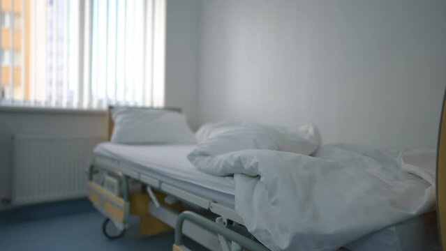 Unmade bed with white clean bedding indoors in medical clinic ward. Live camera panning left to right along modern comfortable furniture in cozy hospital ward. Hygiene and medicine