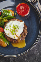Minced beef steak with poached egg and vegetable garnish with tomato sauce on plate