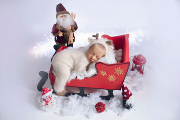 Beautiful newborn baby sleeps in santa claus sleigh dressed as deer