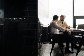 Adult multiracial businessmen using laptop while sitting by table